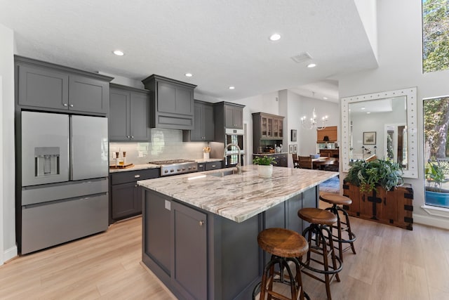 kitchen with a kitchen bar, appliances with stainless steel finishes, a large island with sink, and gray cabinetry