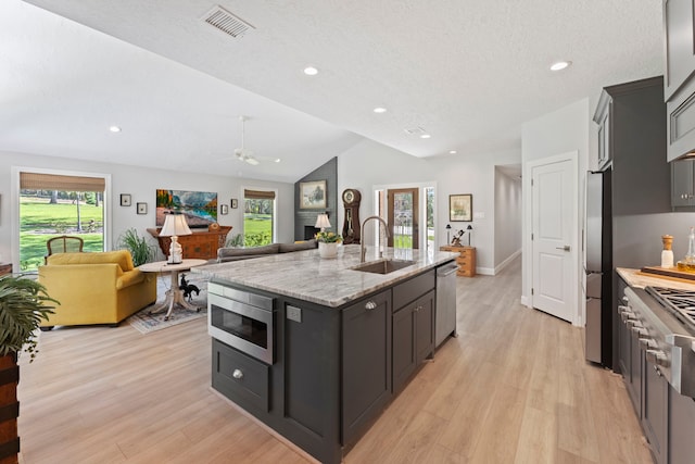 kitchen featuring a kitchen island with sink, stainless steel appliances, plenty of natural light, and vaulted ceiling