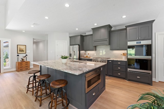 kitchen featuring gray cabinetry, a kitchen island with sink, stainless steel appliances, and light wood-type flooring