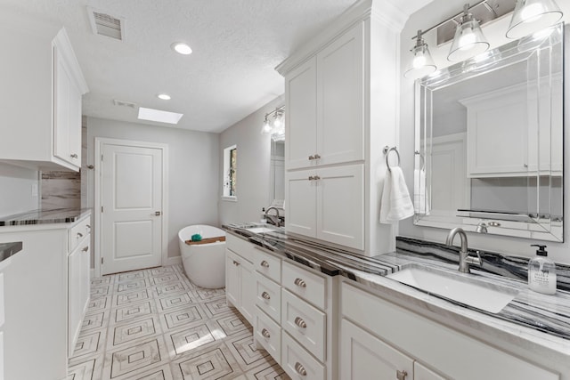 bathroom with a bathtub, vanity, a skylight, and a textured ceiling