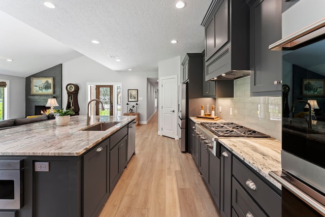 kitchen with sink, a kitchen island with sink, stainless steel appliances, a fireplace, and vaulted ceiling