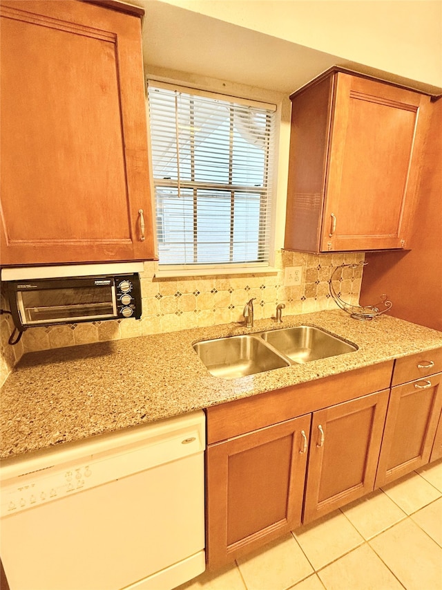 kitchen with tasteful backsplash, light stone countertops, sink, white dishwasher, and light tile patterned floors