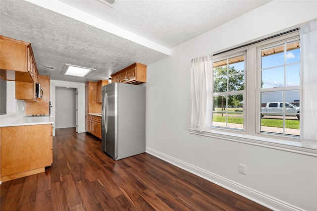 kitchen with appliances with stainless steel finishes, a wealth of natural light, a textured ceiling, and dark hardwood / wood-style flooring