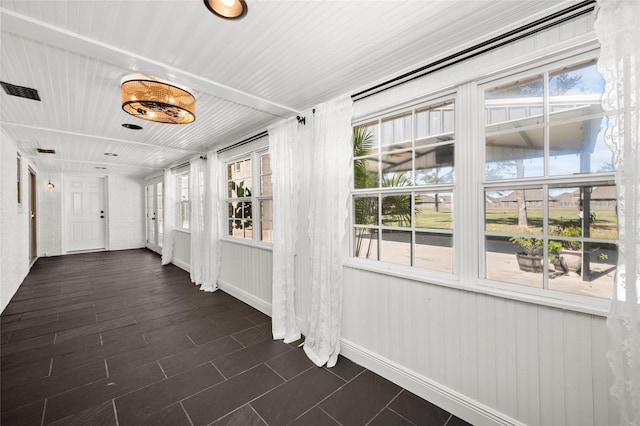 hall featuring visible vents, baseboards, and dark tile patterned flooring