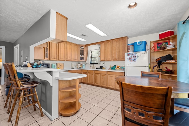 kitchen with a kitchen breakfast bar, kitchen peninsula, white fridge, light tile patterned floors, and a textured ceiling