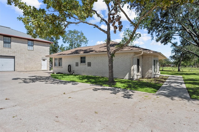 back of house featuring a garage, a yard, brick siding, and driveway