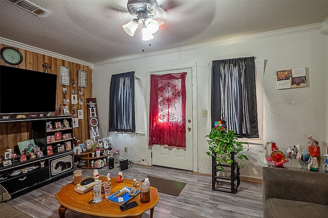 living room featuring hardwood / wood-style flooring, crown molding, ceiling fan, and a textured ceiling