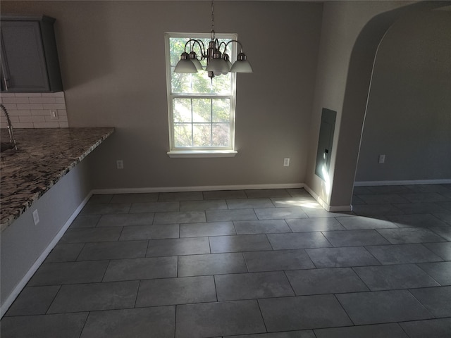 unfurnished dining area featuring a notable chandelier, dark tile patterned flooring, and a wealth of natural light