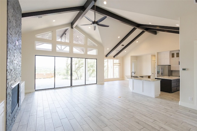 unfurnished living room with beam ceiling, a fireplace, high vaulted ceiling, and ceiling fan