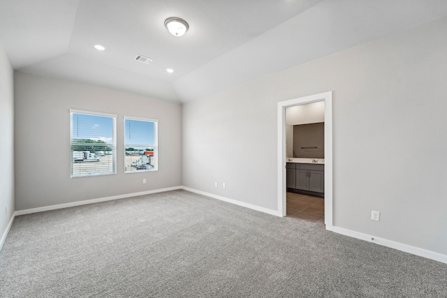 unfurnished bedroom with light colored carpet, ensuite bath, and lofted ceiling