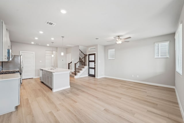 kitchen featuring ceiling fan, sink, pendant lighting, a center island with sink, and light hardwood / wood-style floors