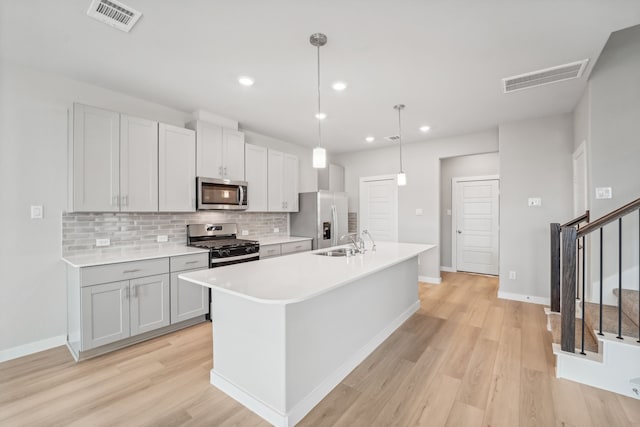 kitchen with stainless steel appliances, sink, light hardwood / wood-style flooring, hanging light fixtures, and an island with sink