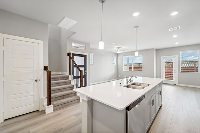 kitchen with stainless steel dishwasher, sink, a center island with sink, light hardwood / wood-style flooring, and hanging light fixtures