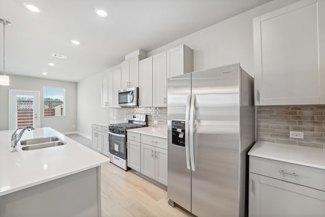 kitchen featuring light wood-type flooring, tasteful backsplash, stainless steel appliances, sink, and decorative light fixtures