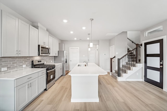 kitchen with light wood-type flooring, stainless steel appliances, a kitchen island with sink, white cabinetry, and hanging light fixtures