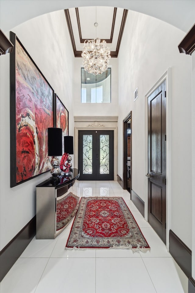 tiled entryway featuring a high ceiling, ornamental molding, french doors, and an inviting chandelier