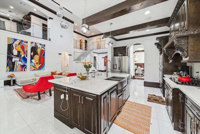 kitchen featuring an island with sink, beamed ceiling, sink, hanging light fixtures, and appliances with stainless steel finishes