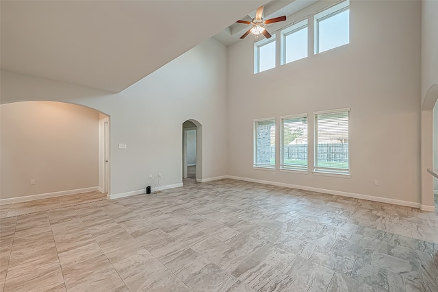 unfurnished living room featuring ceiling fan, a towering ceiling, and a healthy amount of sunlight