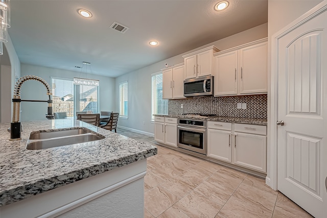 kitchen featuring decorative backsplash, white cabinets, sink, appliances with stainless steel finishes, and decorative light fixtures