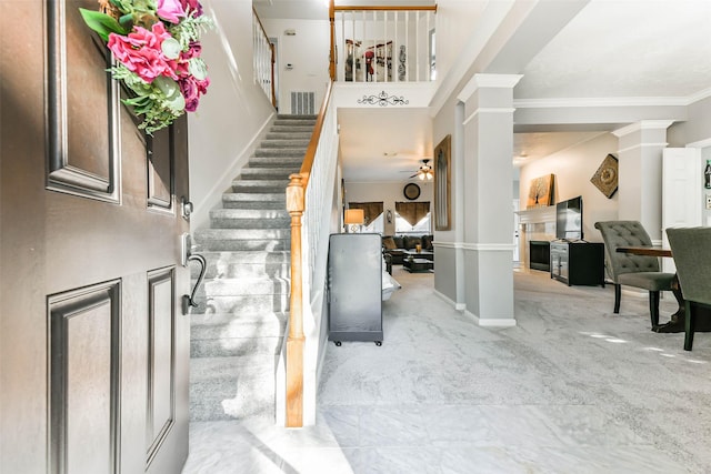 carpeted entrance foyer featuring decorative columns, ceiling fan, and ornamental molding