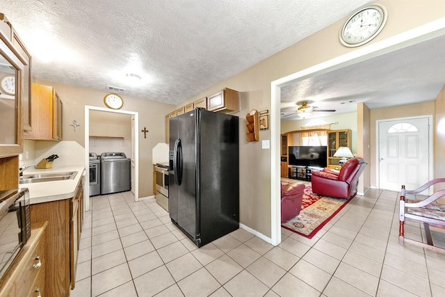 kitchen featuring separate washer and dryer, black fridge with ice dispenser, stainless steel range with electric cooktop, light tile patterned floors, and a textured ceiling