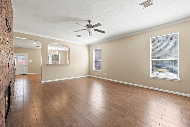 empty room featuring a wealth of natural light, crown molding, ceiling fan with notable chandelier, and a stone fireplace