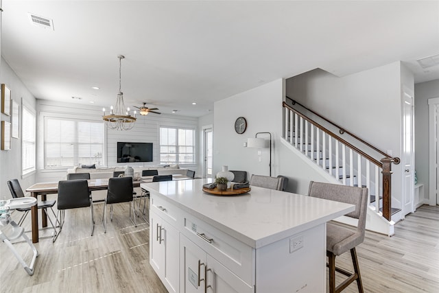 kitchen with light wood-type flooring, a kitchen island, a kitchen breakfast bar, decorative light fixtures, and white cabinets