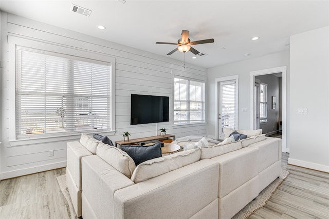 living room with light wood-type flooring, a healthy amount of sunlight, ceiling fan, and wooden walls