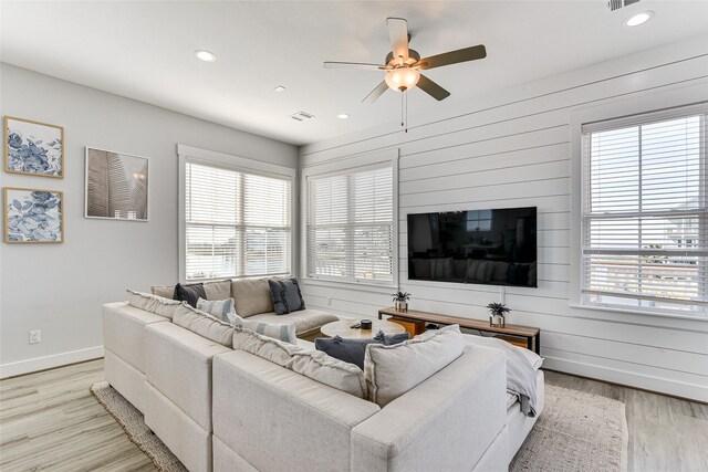 living room featuring wooden walls, light wood-type flooring, and ceiling fan