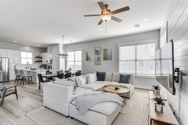 living room with ceiling fan with notable chandelier, light hardwood / wood-style flooring, and a wealth of natural light