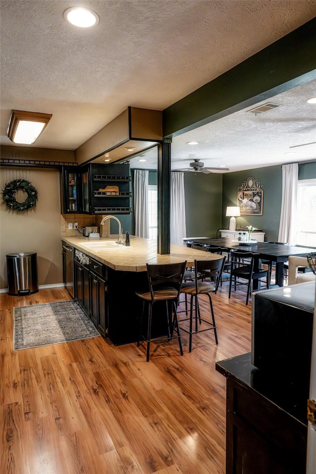 kitchen featuring dishwasher, sink, a textured ceiling, light hardwood / wood-style floors, and a breakfast bar area