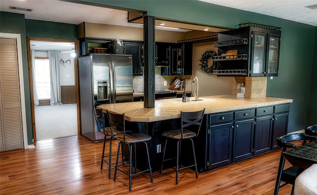 bar featuring stainless steel fridge with ice dispenser, light hardwood / wood-style flooring, tile counters, and sink