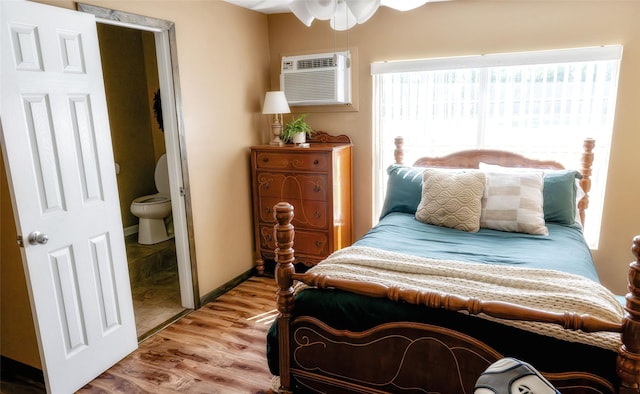 bedroom with hardwood / wood-style floors, an AC wall unit, and connected bathroom