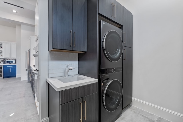 clothes washing area with wine cooler, stacked washer and clothes dryer, cabinets, and sink