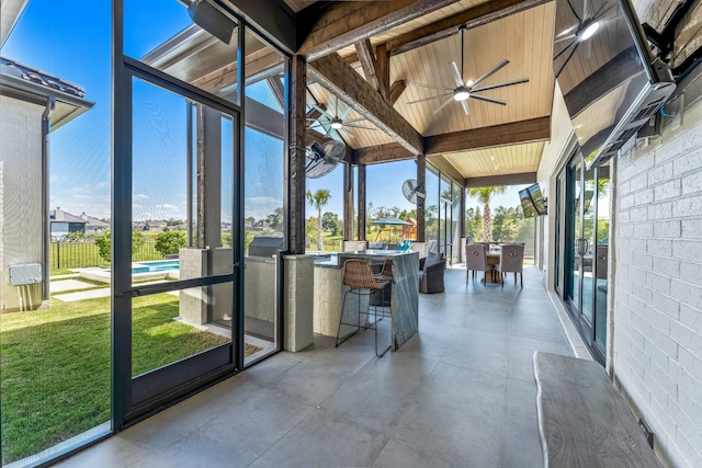 unfurnished sunroom featuring ceiling fan, lofted ceiling with beams, and wooden ceiling