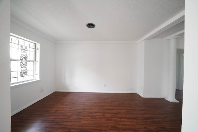 empty room with a textured ceiling, dark hardwood / wood-style floors, ornate columns, and crown molding