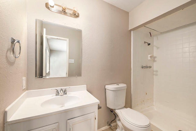 bathroom featuring a tile shower, vanity, and toilet