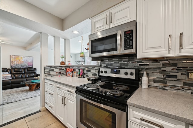 kitchen with light stone countertops, backsplash, white cabinets, appliances with stainless steel finishes, and light tile patterned floors