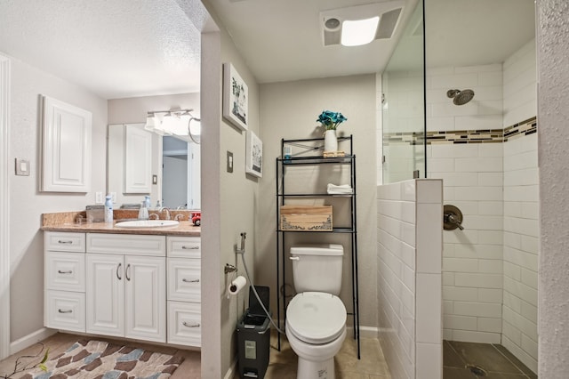 bathroom with a textured ceiling, tiled shower, vanity, and toilet