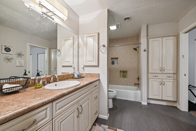 full bathroom featuring vanity, tiled shower / bath combo, toilet, and a textured ceiling