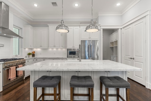 kitchen with built in appliances, a kitchen island with sink, and wall chimney exhaust hood