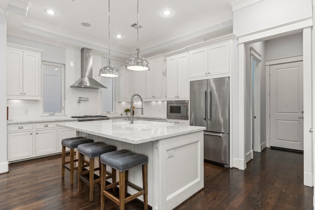 kitchen featuring pendant lighting, an island with sink, white cabinets, built in appliances, and wall chimney exhaust hood