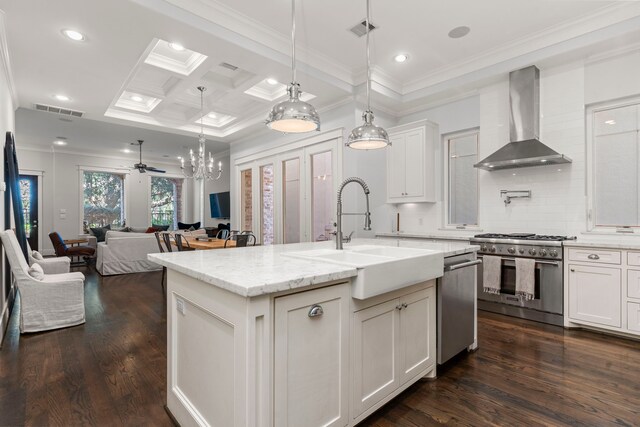 kitchen with appliances with stainless steel finishes, dark hardwood / wood-style flooring, sink, wall chimney range hood, and an island with sink