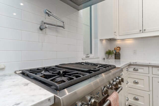 kitchen featuring light stone counters, white cabinetry, stainless steel stove, and tasteful backsplash