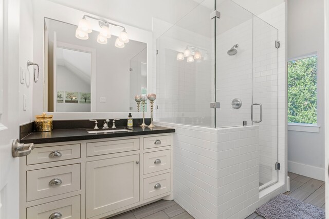 bathroom with vanity, hardwood / wood-style flooring, vaulted ceiling, and a shower with shower door