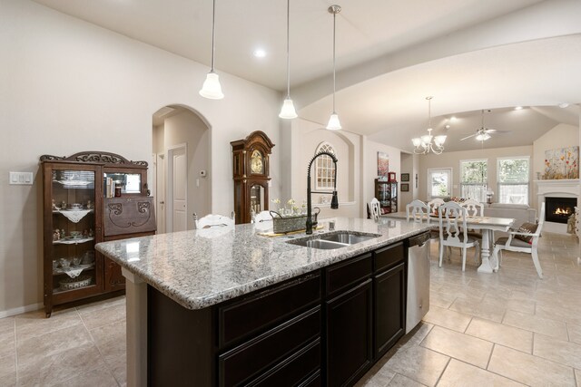 kitchen with lofted ceiling, hanging light fixtures, light stone counters, a kitchen island with sink, and sink