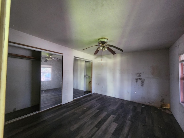 unfurnished bedroom with dark wood-type flooring, multiple closets, and ceiling fan