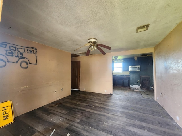 unfurnished living room featuring ceiling fan, dark hardwood / wood-style flooring, a textured ceiling, and a wood stove