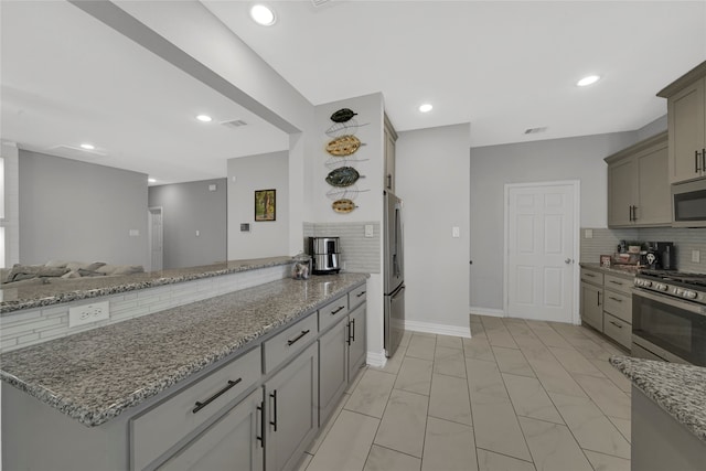 kitchen with light stone counters, stainless steel appliances, gray cabinetry, kitchen peninsula, and backsplash