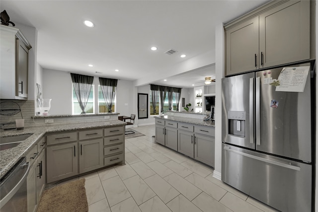 kitchen with appliances with stainless steel finishes, gray cabinets, light stone counters, and backsplash